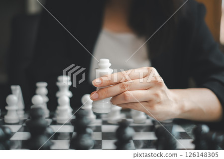 Close-up of a hand holding a chess piece during a strategic game, emphasizing focus and strategy. 126148305
