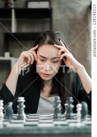 A woman deeply focused on a chess game, contemplating her next move in a modern interior setting. A woman deeply focused on a chess game, contemplating her next move in a modern interior setting. 126148313