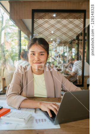 A young woman in a cafe working on her laptop, surrounded by modern decor and natural light. A young woman in a cafe working on her laptop, surrounded by modern decor and natural light. 126148328