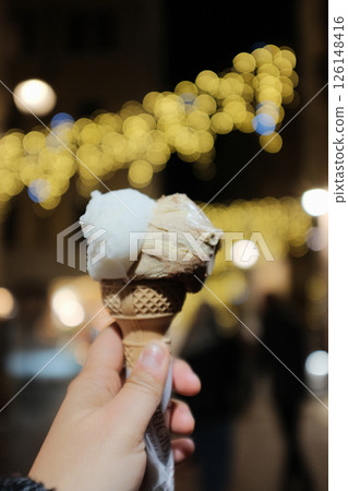 Italian gelato close up in hand and shop scene at Rome night market with decorative lights and festive crowd. High quality photo 126148416