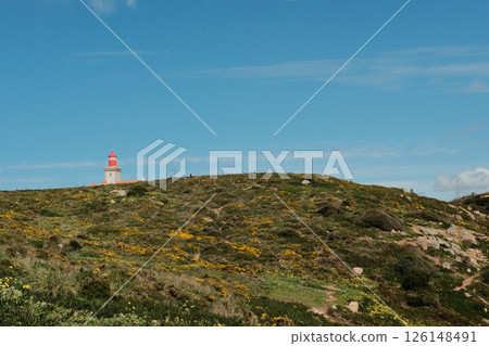 Lush green hills and rugged terrain with blue sky and scattered clouds in Cabo da Roca Sintra Portugal natural landscape with vegetation from scenic hiking trail Lush green hills and rugged terrain with blue sky and scattered clouds in Cabo da Roca Sintra Portugal natural landscape with vegetation from scenic hiking trail 126148491