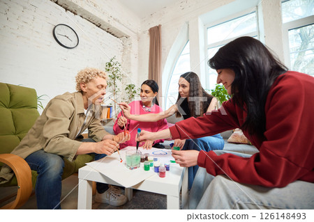 Group of friends painting together at coffee table in bright room, enjoying creative leisure. Group of friends painting together at coffee table in bright room, enjoying creative leisure. 126148493