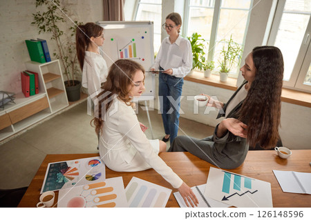 Business team reviews charts and documents with colleague presenting on whiteboard in bright office, discussing performance. Business team reviews charts and documents with colleague presenting on whiteboard in bright office, discussing performance. 126148596