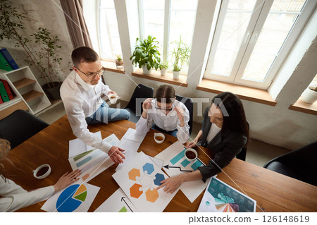 Top view of business team analyzing data and charts at wooden table in modern office, focused on details. Top view of business team analyzing data and charts at wooden table in modern office, focused on details. 126148619