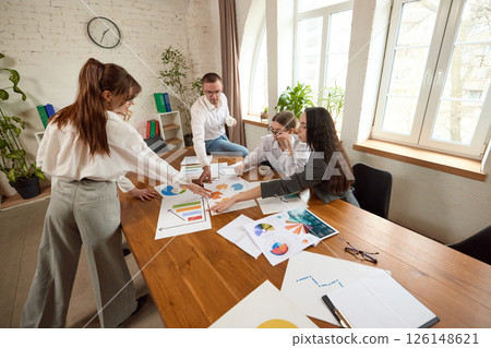 Business team analyzes charts and documents at wooden table in modern office, discussing data with focus. Business team analyzes charts and documents at wooden table in modern office, discussing data with focus. 126148621