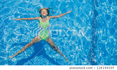 Young girl enjoys a joyful moment while floating in a bright blue swimming pool on a sunny day Young girl enjoys a joyful moment while floating in a bright blue swimming pool on a sunny day 126149105