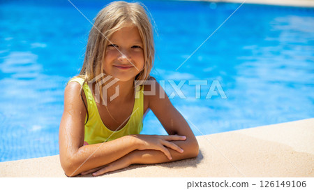 Portrait of smiling child girl enjoys sunny day by the pool in a vibrant yellow swimsuit Portrait of smiling child girl enjoys sunny day by the pool in a vibrant yellow swimsuit 126149106