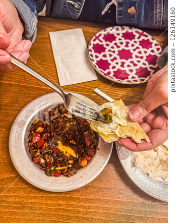 Hands holding fork and bread with delicious meal on table with colorful plate and napkin. High quality photo 126149160