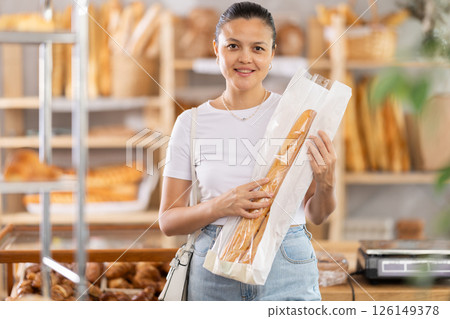 Middle-aged woman holding baguettes in paper bag in bakery 126149378
