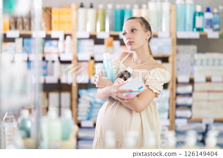 Happy young pregnant woman with full arms choosing something in drugstore 126149404