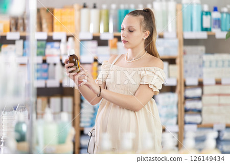 Pregnant woman customer choosing syrup in drugstore Pregnant woman customer choosing syrup in drugstore 126149434