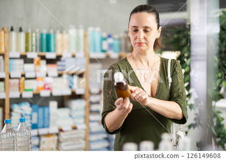 Middle-aged woman customer choosing syrup in drugstore Middle-aged woman customer choosing syrup in drugstore 126149608