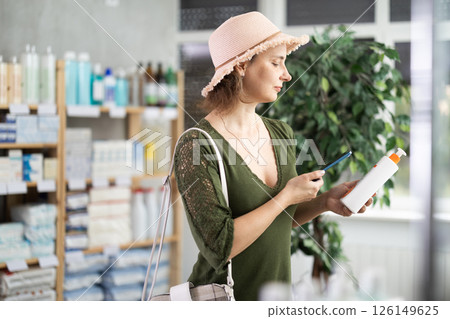 Woman scanning the barcode of a package with SPF cream in a pharmacy Woman scanning the barcode of a package with SPF cream in a pharmacy 126149625