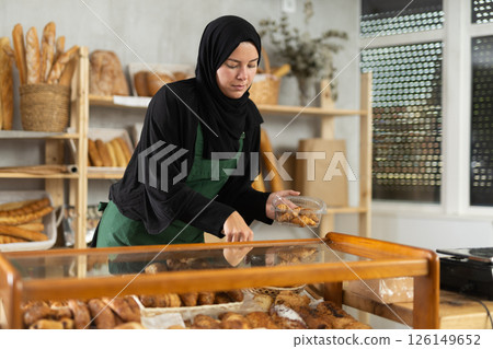 Saleswoman in a hijab collects pastries in a container Saleswoman in a hijab collects pastries in a container 126149652