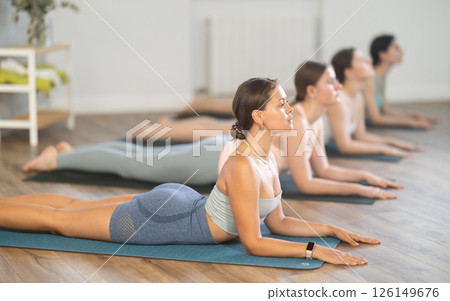 Young girl teaches yoga lesson, shows students technique of performing Urdhva Mukha Shvanasana asana 126149676
