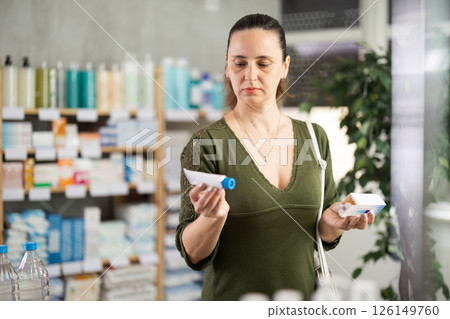 Woman in cardigan choosing ointment at pharmacy Woman in cardigan choosing ointment at pharmacy 126149760