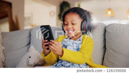 Mobile, headphones and happy child on sofa for music, online learning or play game for education. Girl, audio and kid with phone in home living room for internet app, streaming cartoon or watch video 126150088