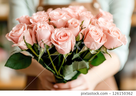 Pink roses bouquet held by florist in a cozy flower shop with warm ambiance and soft lighting Pink roses bouquet held by florist in a cozy flower shop with warm ambiance and soft lighting 126150362