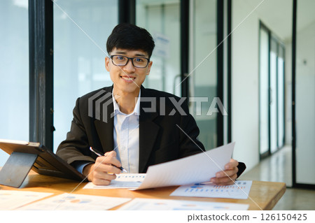 Confident business consultant reviewing financial data and investment plans at office desk 126150425