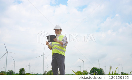 Engineer working with laptop at wind turbine field generating electricity for renewable clean energy 126150565