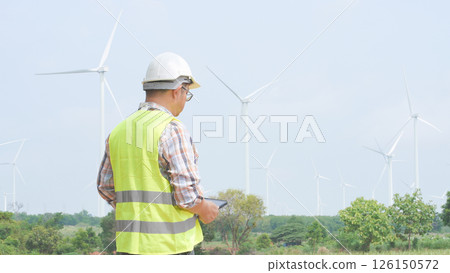 Engineer monitoring windmill performance with tablet at renewable energy field on a bright sunny day 126150572