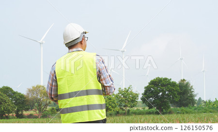 Engineer surveying windmill field for renewable energy operations in rural area on bright sunny day Engineer surveying windmill field for renewable energy operations in rural area on bright sunny day 126150576