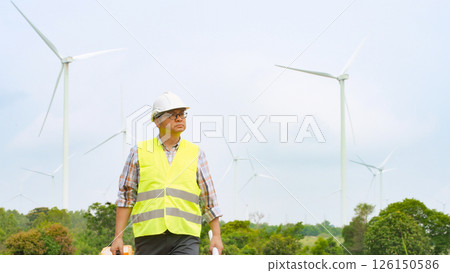 Engineer walking through wind farm with toolbox and blueprint for renewable energy maintenance and inspection Engineer walking through wind farm with toolbox and blueprint for renewable energy maintenance and inspection 126150586