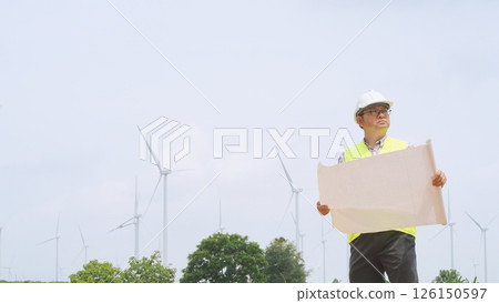 Engineer holding blueprint while surveying wind turbines at renewable energy site under bright sky conditions. Engineer holding blueprint while surveying wind turbines at renewable energy site under bright sky conditions. 126150597