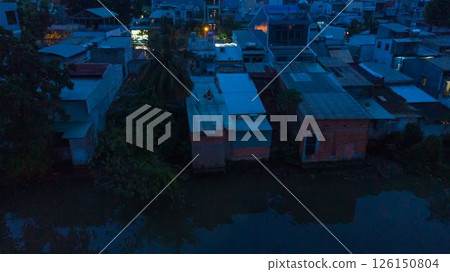 Aerial view of illuminated church by river surrounded by high rise residential buildings and city streets during blue hour with urban skyline and canal cityscape at twilight. High quality photo 126150804