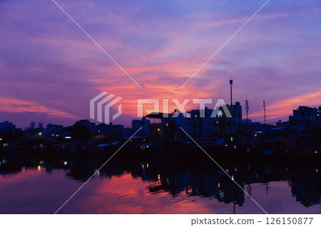 Stunning pink and purple sunset sky reflecting on calm river with silhouetted city skyline and peaceful twilight atmosphere in urban landscape at dusk. High quality photo Stunning pink and purple sunset sky reflecting on calm river with silhouetted city skyline and peaceful twilight atmosphere in urban landscape at dusk. High quality photo 126150877
