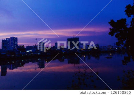 Stunning pink and purple sunset sky reflecting on calm river with silhouetted city skyline and peaceful twilight atmosphere in urban landscape at dusk. High quality photo 126150890