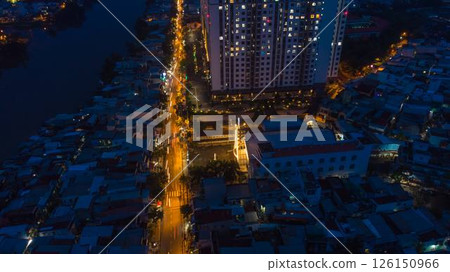 Aerial view of illuminated church by river surrounded by high rise residential buildings and city streets during blue hour with urban skyline and canal cityscape at twilight. High quality photo 126150966