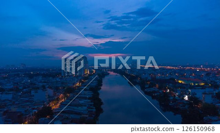 Aerial view of illuminated church by river surrounded by high rise residential buildings and city streets during blue hour with urban skyline and canal cityscape at twilight. High quality photo 126150968