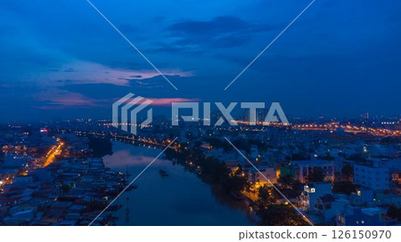 Aerial view of illuminated church by river surrounded by high rise residential buildings and city streets during blue hour with urban skyline and canal cityscape at twilight. High quality photo 126150970