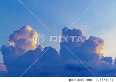 Towering cumulus clouds glowing in golden sunlight against clear blue sky at sunset with dramatic natural cloudscape and atmospheric light. High quality photo 126151075