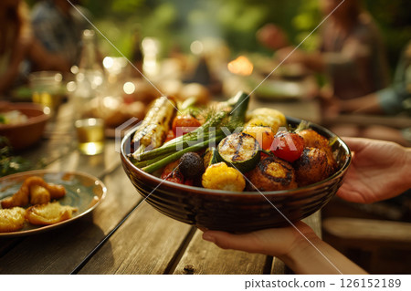 Bowl of grilled veggies handed over at al fresco gathering 126152189