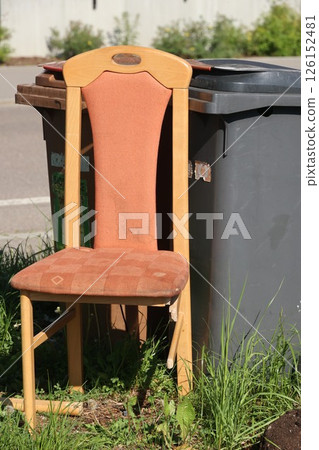 A chair is sitting on the grass next to a trash can A chair is sitting on the grass next to a trash can 126152481