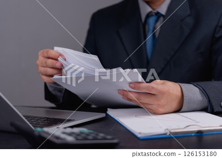 Businessman reviewing financial documents and reports. Office paperwork, data analysis, corporate management, financial review, business planning, and accounting operations. Businessman reviewing financial documents and reports. Office paperwork, data analysis, corporate management, financial review, business planning, and accounting operations. 126153180