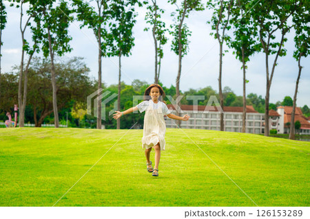 A cute and happy little girl is playing and running around the park on a beautiful morning. 126153289