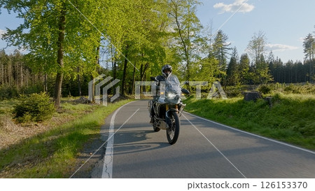 Driver riding motorcycle on empty asphalt road, spring mountains during sunset Driver riding motorcycle on empty asphalt road, spring mountains during sunset 126153370