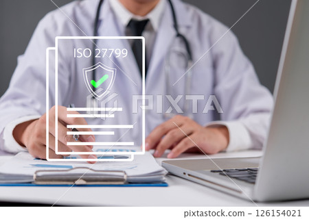 A doctor working on medical documents with an ISO 27799 security certification icon, symbolizing healthcare data protection. 126154021