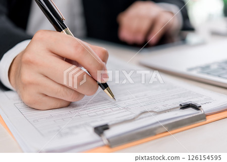 Business and financial paperwork verification featuring a close-up of hands working on a contract. Ideal for corporate, investment, and legal consulting. Business and financial paperwork verification featuring a close-up of hands working on a contract. Ideal for corporate, investment, and legal consulting. 126154595