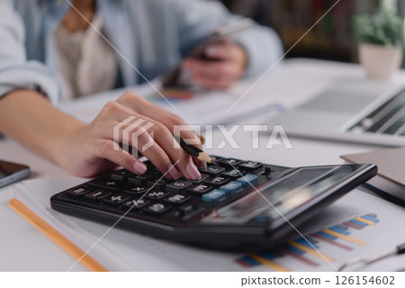 Woman using calculator with financial documents on table, representing accounting, tax calculation, personal finance, budgeting, and small business management. 126154602
