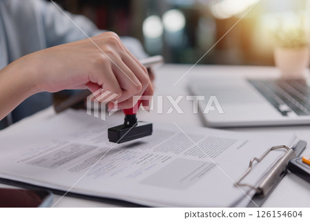 Close-up of hand using a red stamp on a legal document, indicating confirmation or validation in administrative work. 126154604