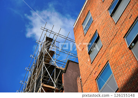 Looking up steel pipe scaffolding next to orange brick building against blue sky 126155148