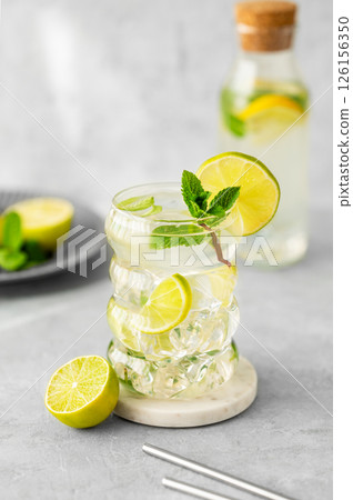 Mojito cocktail in a glass with lime, mint and ice on a textured background with natural light Mojito cocktail in a glass with lime, mint and ice on a textured background with natural light 126156350