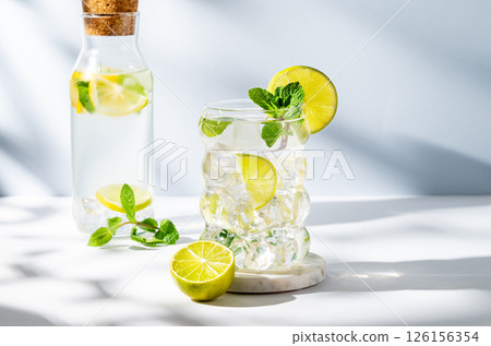 Mojito cocktail in a glass with lime, mint and ice on a white blue background with shadow and bottle 126156354