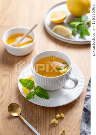 Cup of herbal tea with lemon, honey and mint on wooden tabletop with citrus fruits 126156368