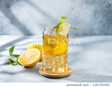 Iced drink with lemon and mint in a glass on a light background with shadows and citrus fruits. Iced drink with lemon and mint in a glass on a light background with shadows and citrus fruits. 126156369