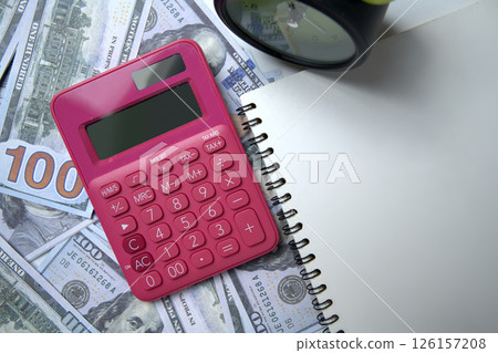 Top view of a pink calculator and a pile of 100 dollar banknotes with an alarm clock and a notebook. Copy space. Concept of wealth, saving or investment, and tax 126157208